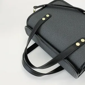 Détail d'un sac à main gris tissé élégant avec des sangles en cuir noir et des rivets.