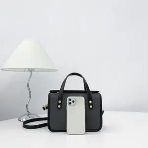 Détail d'un sac à main carré minimaliste gris avec un smartphone pour référence de taille