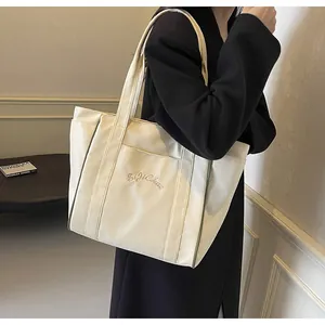 Vista detallada de un bolso tote de nailon crema con bordado elegante y correas fuertes.