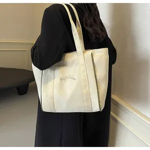 Vista detallada de un bolso tote de nailon beige con bordado, colgado del hombro