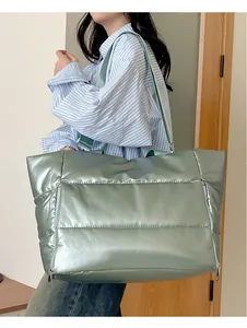 Close-up lifestyle view of large metallic sage green puffer travel bag on shoulder.