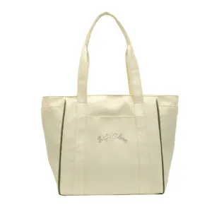 Vista frontal de un bolso tote de nailon crema con ribetes verdes y bordado