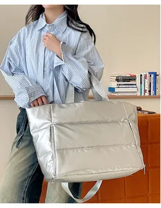 Large silver metallic puffer travel bag shown on a model in a stylish home setting