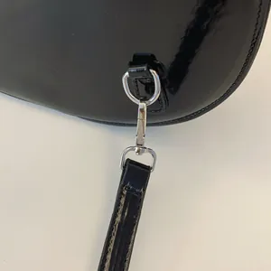 Close-up of silver metal clasp on black glossy patent leather shoulder bag detail