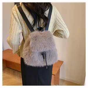 Detail of a grey faux fur bucket backpack shown on a model wearing a cream sweater