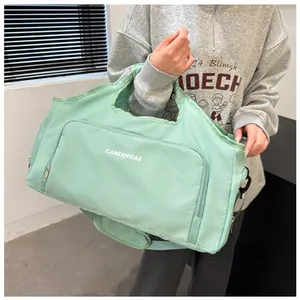 Mint green travel duffel bag shown as a crossbody bag held by a person indoors.