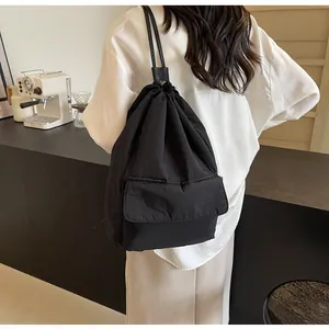 Detail view of a black lightweight nylon drawstring backpack worn by a person