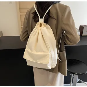 Detailed back view of a minimalist cream nylon drawstring backpack worn by a model in a cafe.