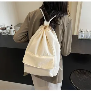 Back view of model wearing the large cream nylon drawstring backpack in a cafe setting.