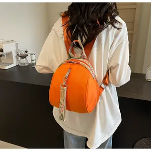 Mini sac à dos orange en forme de coquillage porté par un mannequin dans un café chic