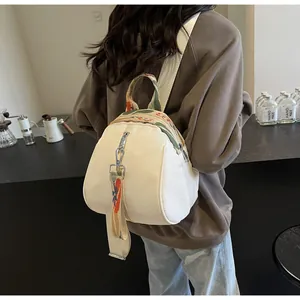 Petit sac à dos en nylon beige en forme de coquille porté par un mannequin au café.