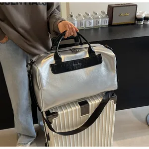Primer plano de un bolso de viaje plateado metalizado sobre una maleta blanca con asas.