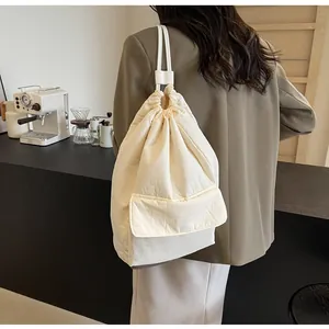 Minimalist cream nylon drawstring bucket backpack for women shown on model in a cafe setting