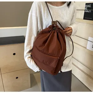 Brown lightweight nylon drawstring bucket backpack worn by a model in minimalist room