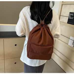 Detail view of brown nylon drawstring backpack worn by model in minimalist setting