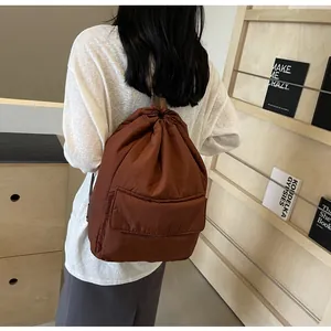Rear view of minimalist brown nylon drawstring backpack worn over a white shirt.