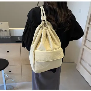 Detailed view of cream nylon drawstring backpack worn by model in minimalist setting