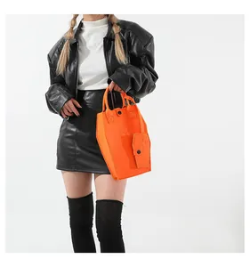Close-up of a unique orange coffin-shaped handbag set held by a model in black leather outfit.