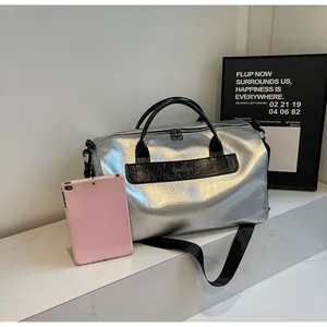 Vista detallada de una gran bolsa de viaje plateada metálica junto a una tableta rosa