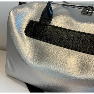 Detalle de bolsa de deporte plateada metalizada con logo Noco Bag y textura arrugada.