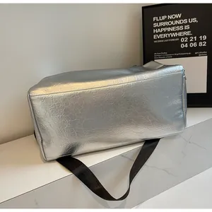 Primer plano de un bolso de viaje plateado con superficie texturizada y correa negra