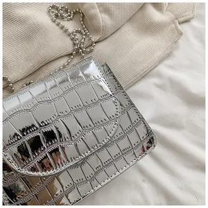 Primo piano di una mini borsa a tracolla argento con motivo coccodrillo e catena.