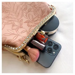 Detail van roze handtas met bloemenreliëf, diamanten frame en cosmetica-inhoud