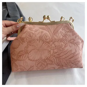 Gedetailleerde close-up van een roze handtas met vintage bloemenreliëf en metalen sluiting.