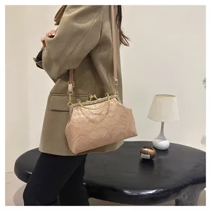 Detailopname van beige handtas met bloemenreliëf en strass-beugelsluiting.