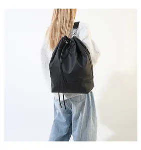 Frau mit schwarzem Rucksack mit Kordelzug über einem grauen Pullover im Studio.