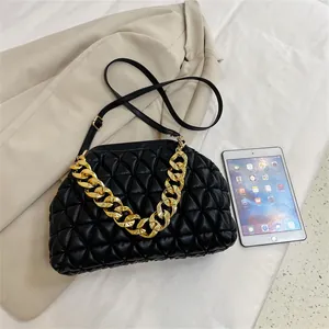 Schwarze gesteppte Tasche mit goldener Kette und Schultergurt auf hellem Stoffhintergrund
