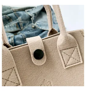 Close-up of the black button closure and reinforced stitching on a beige felt tote bag.