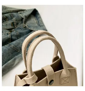 Detailed macro view of beige felt tote bag handles and metallic snap button closure