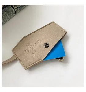 Close-up detail of beige felt card holder with embossed cross design and metal snap button