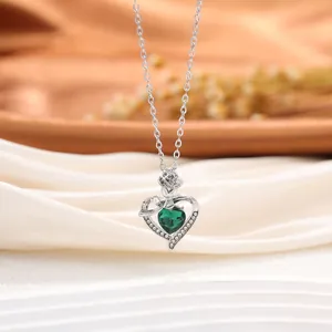 Vue macro détaillée d'un collier pendentif cœur en argent avec cristal vert et motif de rose.