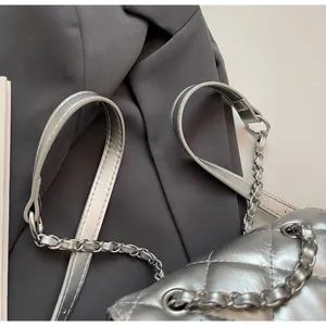 Détail d'un sac seau matelassé argenté montrant la texture métallique et les chaînes.