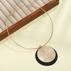 Primer plano de colgante circular metálico en oro y negro sobre gargantilla dorada chic.