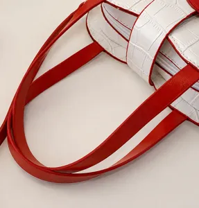 Close-up of red leather handles and white croc-embossed texture of a handbag.