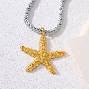 Close-up of golden starfish pendant with detailed metallic texture and silver braided cord