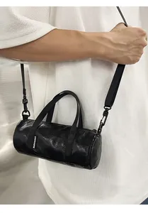 Professional close-up of a mini black cylindrical crossbody bag held by a model.