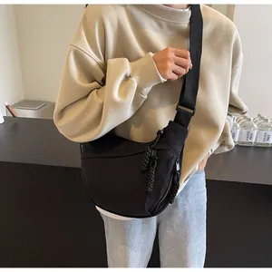 Detail of a black canvas dumpling crossbody bag on model, featuring woven zipper pulls.