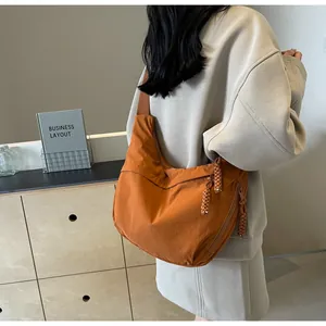 Side view of a casual orange canvas dumpling crossbody bag worn by a model in a room