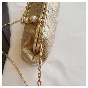 Close-up of golden chain and pearl beaded handle on an elegant lace clutch handbag.