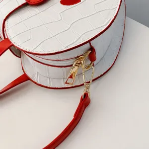 Detail of the shiny gold-toned hardware hook on a white crocodile patterned handbag