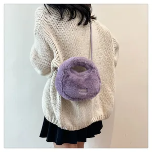 Detalle de un bolso bandolera de peluche morado llevado con un jersey de punto grueso.