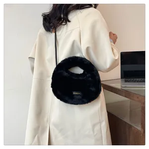 Bolso de mano negro de piel sintética estilo dumpling llevado con gabardina beige.