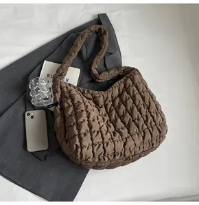 Close-up detail of a brown quilted bubble tote bag on a gray blazer and white sheet