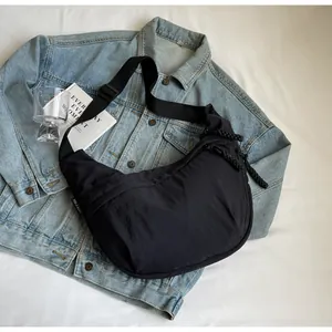 Close-up view of a black crescent-shaped nylon crossbody bag styled on a blue denim jacket