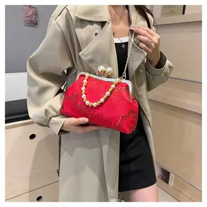 Close-up of elegant red silk handbag featuring pearl beaded handle and gold chain strap