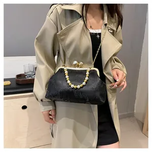 Model carrying a black embroidered clutch bag with pearl handle and gold chain